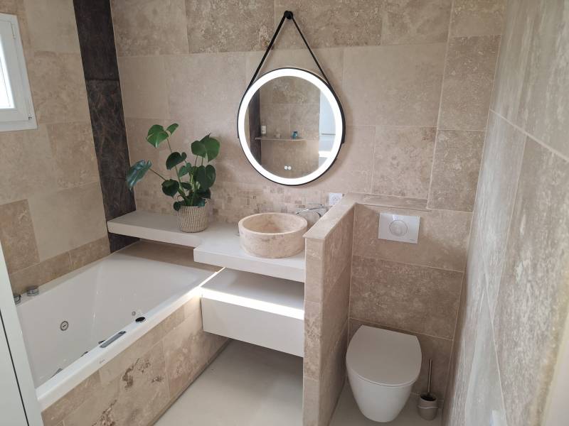 Salle de bain en travertin beige avec baignoire balneo par Chauff'o plombier dans l'Eure